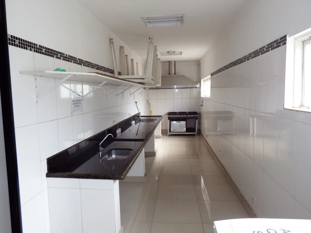 Cozinha de apoio do salão com bancada de granito, duas pias, fogão industrial e coifa