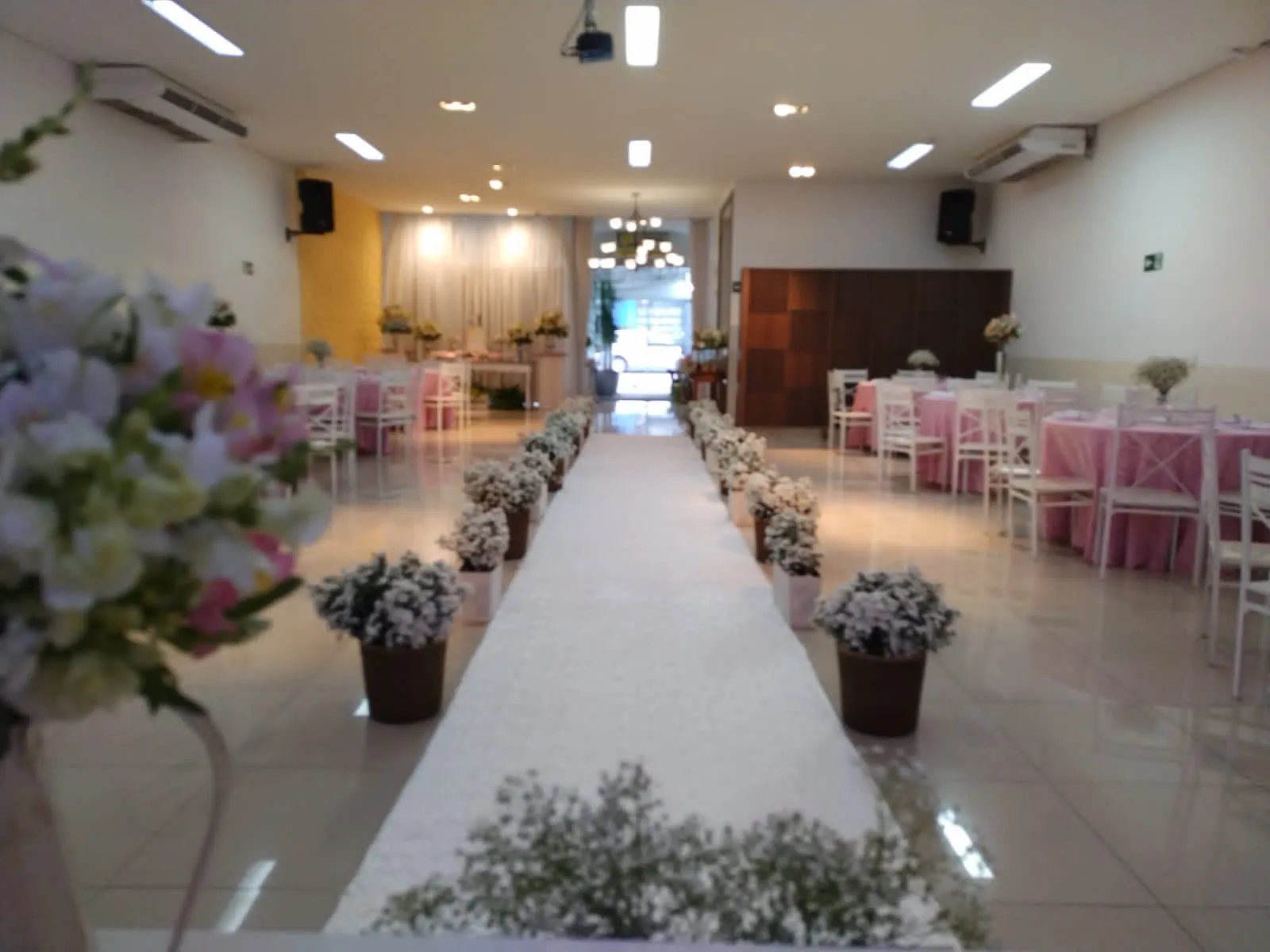 Passarela de cerimônia com vasos de flores e mesas decoradas em rosa ao lado